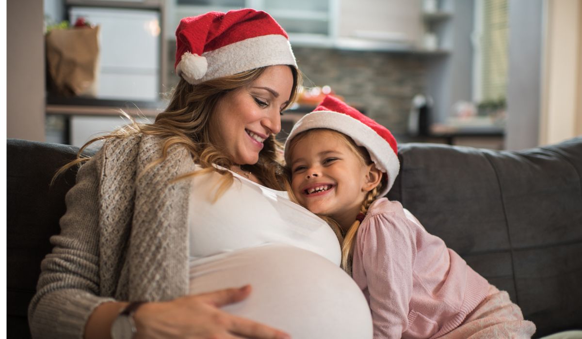 Woman pregnant at Christmas with another child hugging her