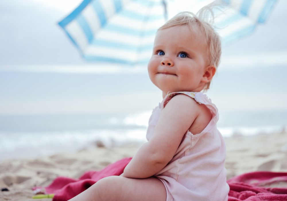 Young girl in a pink top sitting under an umbrella at the beach
