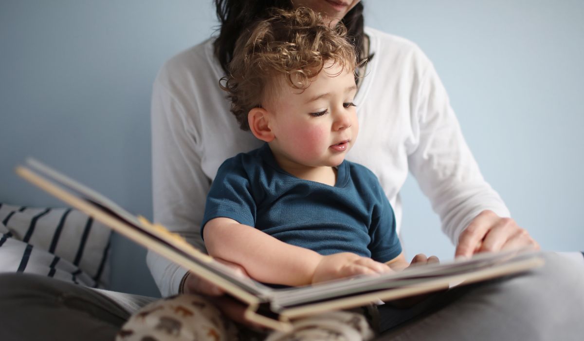 Little boy sitting on his mother's lap reading a book