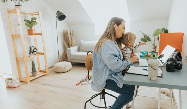 Mum with a toddler sitting on her lap while she's at a laptop
