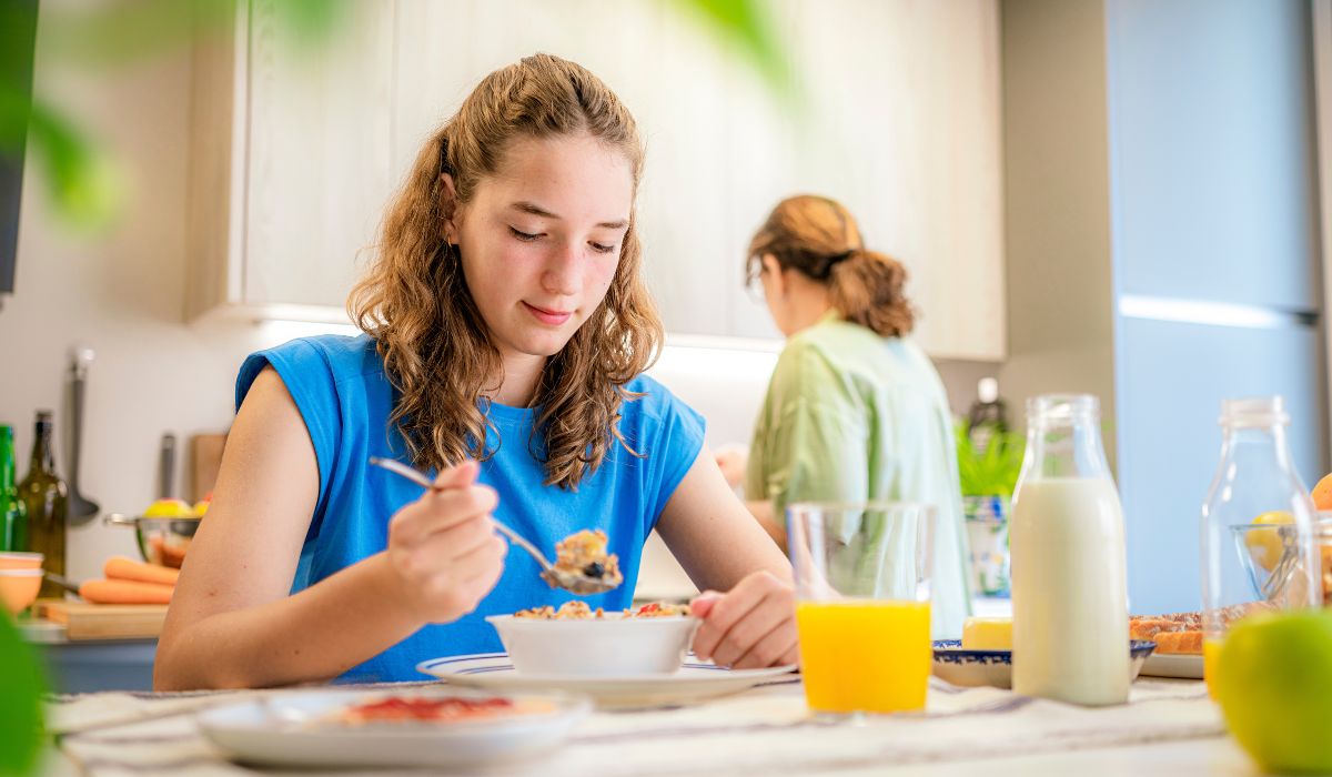 Teenager eating breakfast with her mum in the background