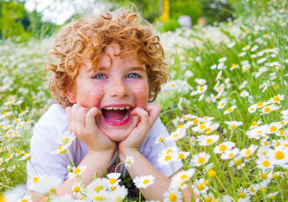 Boy sitting in a field of daisy's with red curly hair