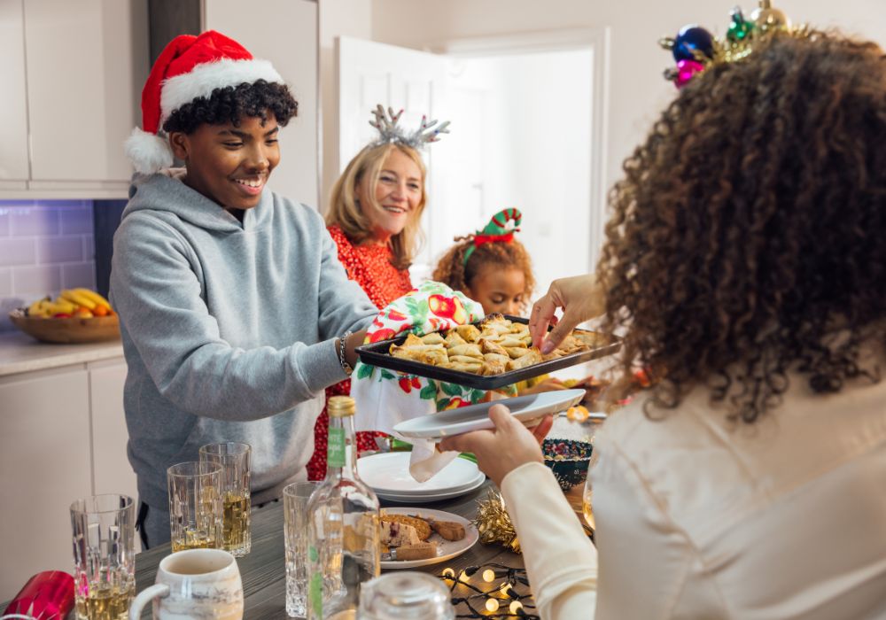 Teenage boy wearing Christmas hat passing baked cookies to woman