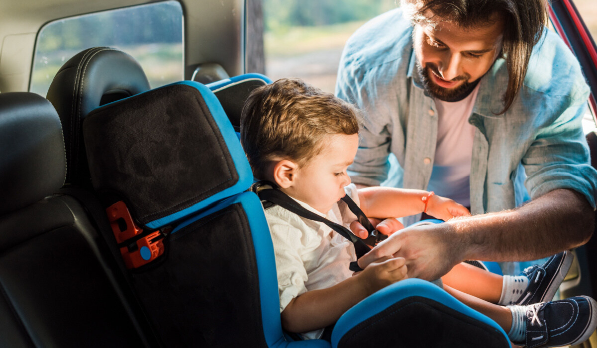 Young father strapping toddler into car seat