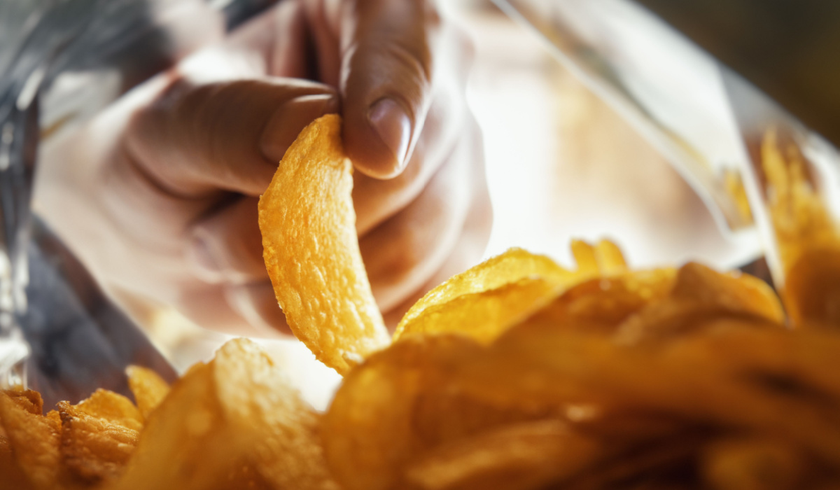 Hand grabbing crisps in open packet of crisps