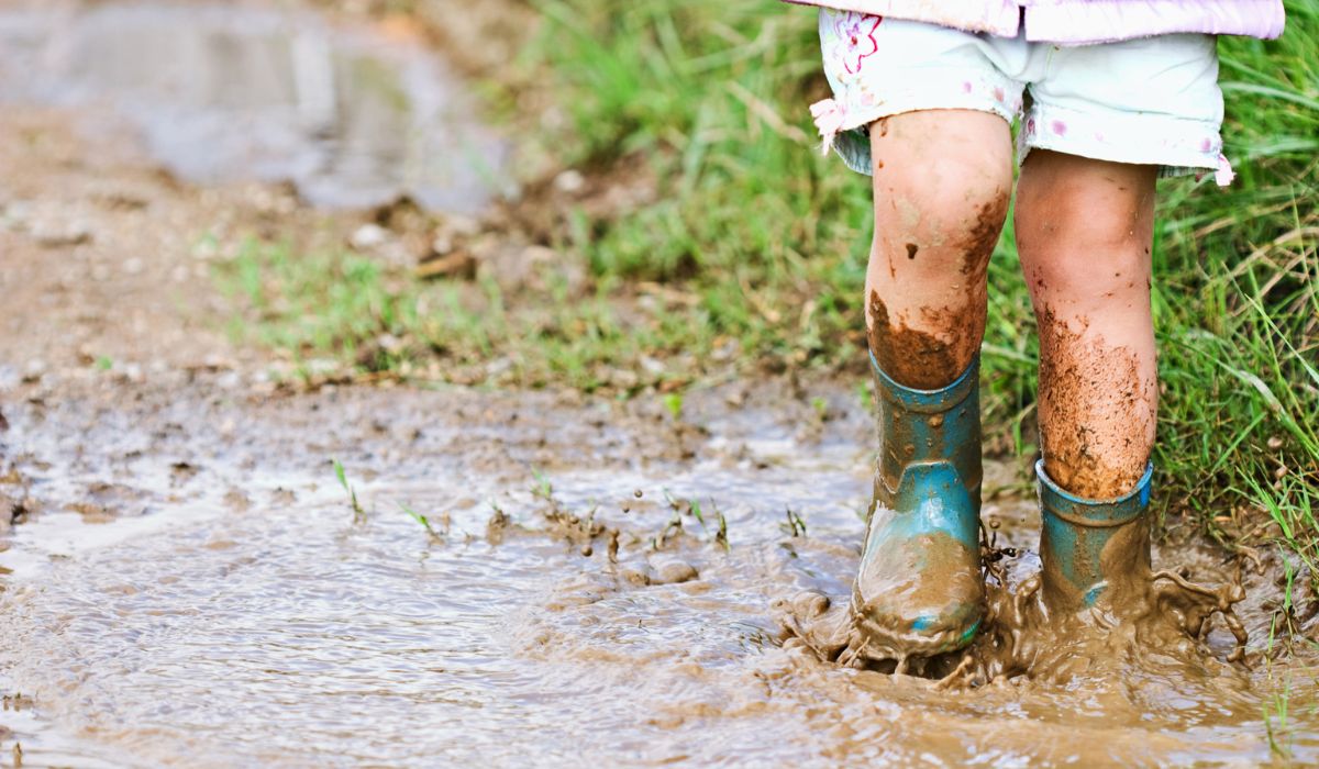 Child jumping in muddy puddle