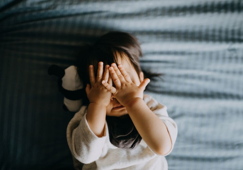 Baby lying in cot with hands covering eyes