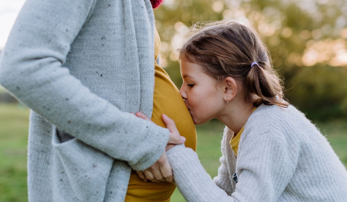 Daughter kissing mother's baby bump
