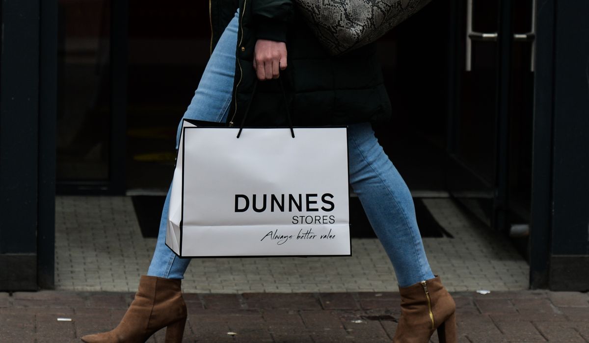 Woman in jeans and brown boots walking holding a Dunnes Stores bag