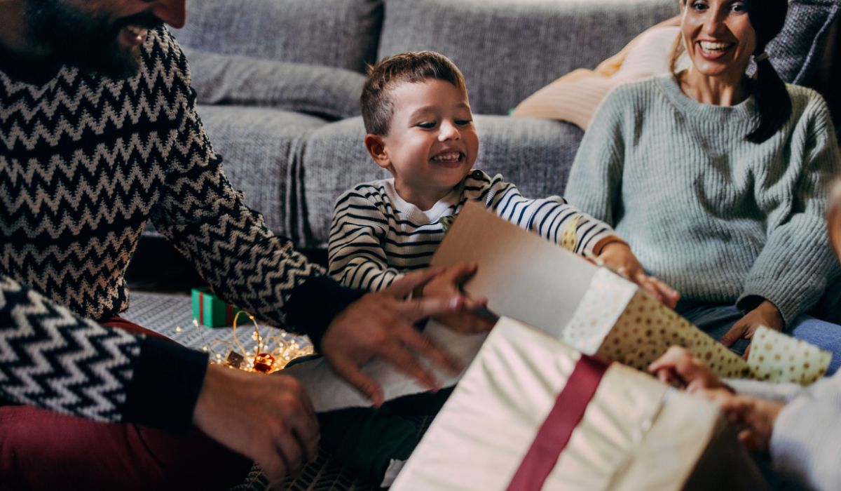 Little boy opening Christmas gifts on the couch with his parents