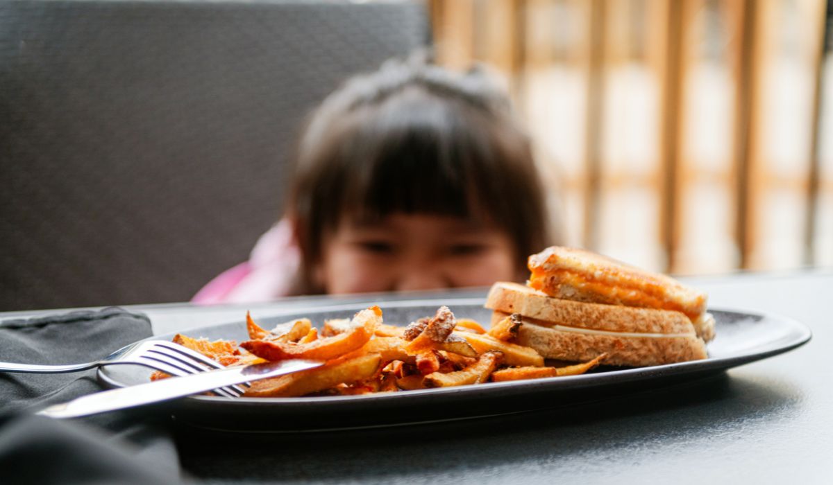 Little girl hiding behind a dish on a dining table.