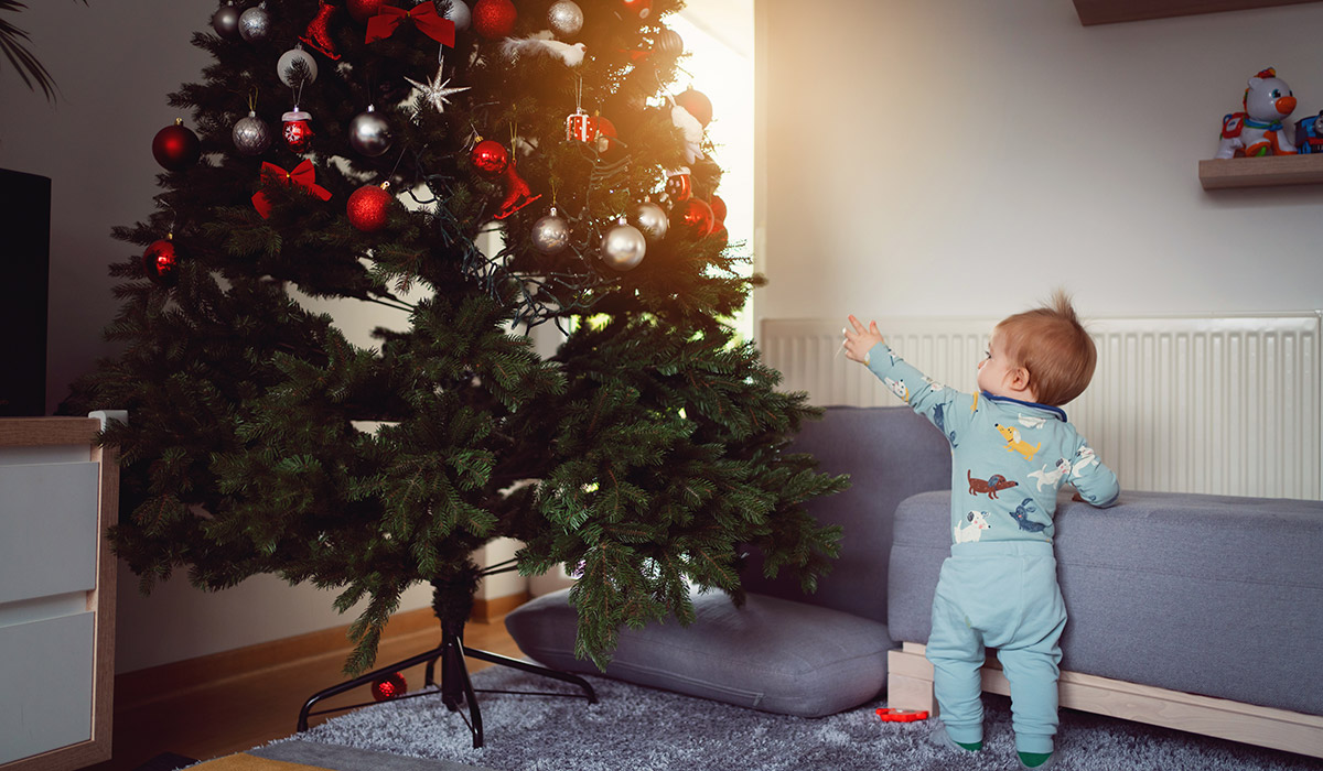Baby boy standing and holding on to the sofa while pointing at the Christmas tree. Pic: Getty Images