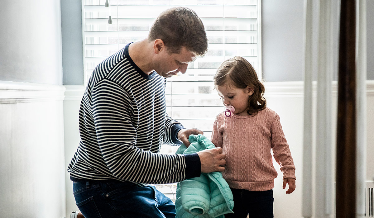 Father getting daughter dressed to go outside