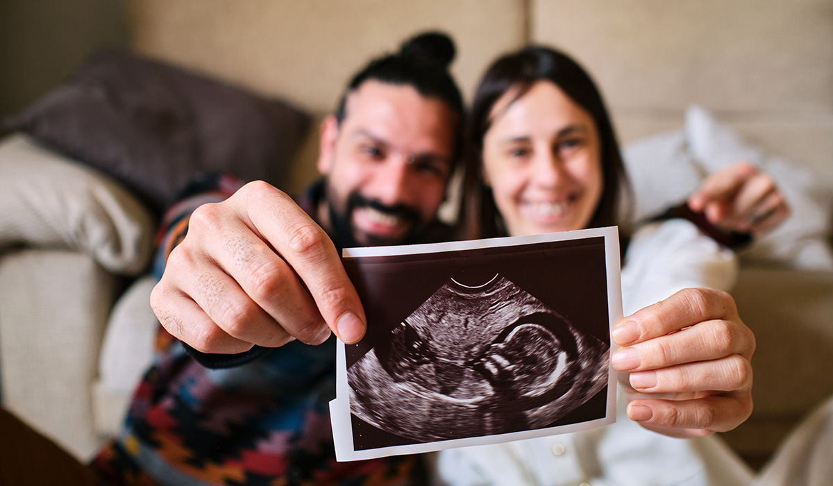 Couple sitting on the floor happily and excitedly show the camera the ultrasound of the baby they are expecting.