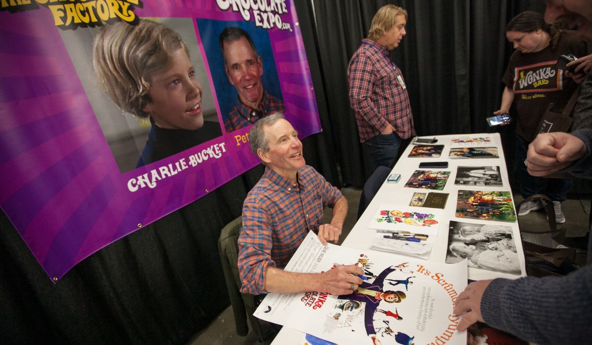 Peter Ostrum signs an autograph for attendees during an event related to the film 'Willie Wonka and the Chocolate Factory
