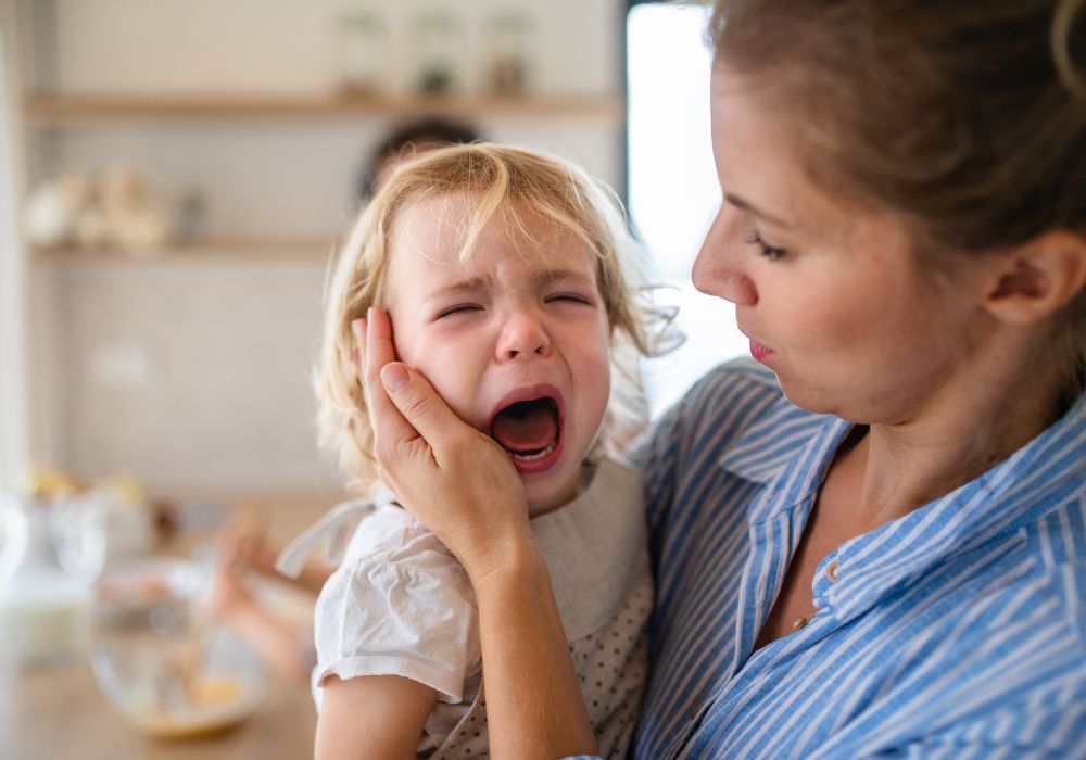 A woman holding the face of her crying toddler