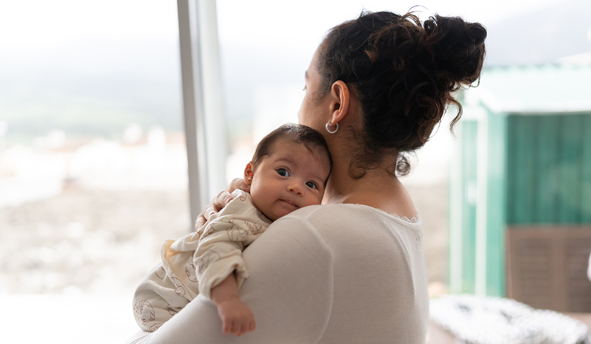 the mother is on her back looking out the window while holding the baby in her arms. The baby is looking at the camera. Concept of protection