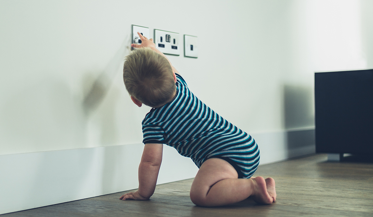 A little baby is reaching for a plug socket at home not knowing the danger
