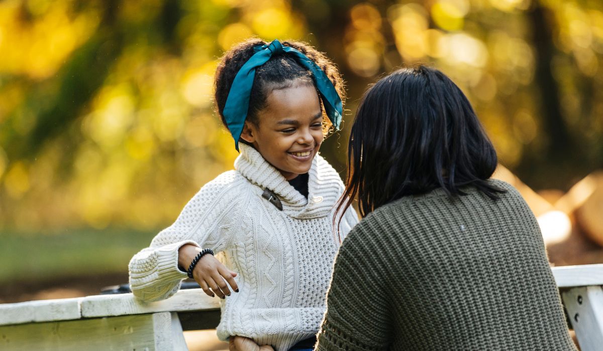 Woman talking to little girl who is smiling and wearing a blue bow in her hair