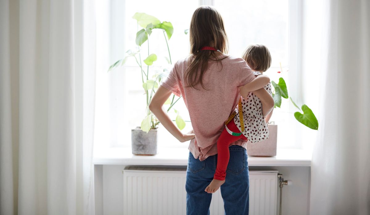 Mother holding child on hip and looking out window