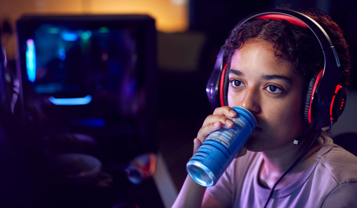 Teenage girl drinking energy drink and playing video game