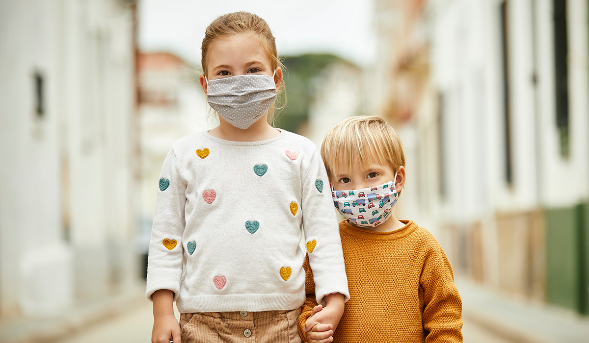 Portrait of little girl and little boy on the street holding hands and wearing home made masks for coronavirus pandemic.