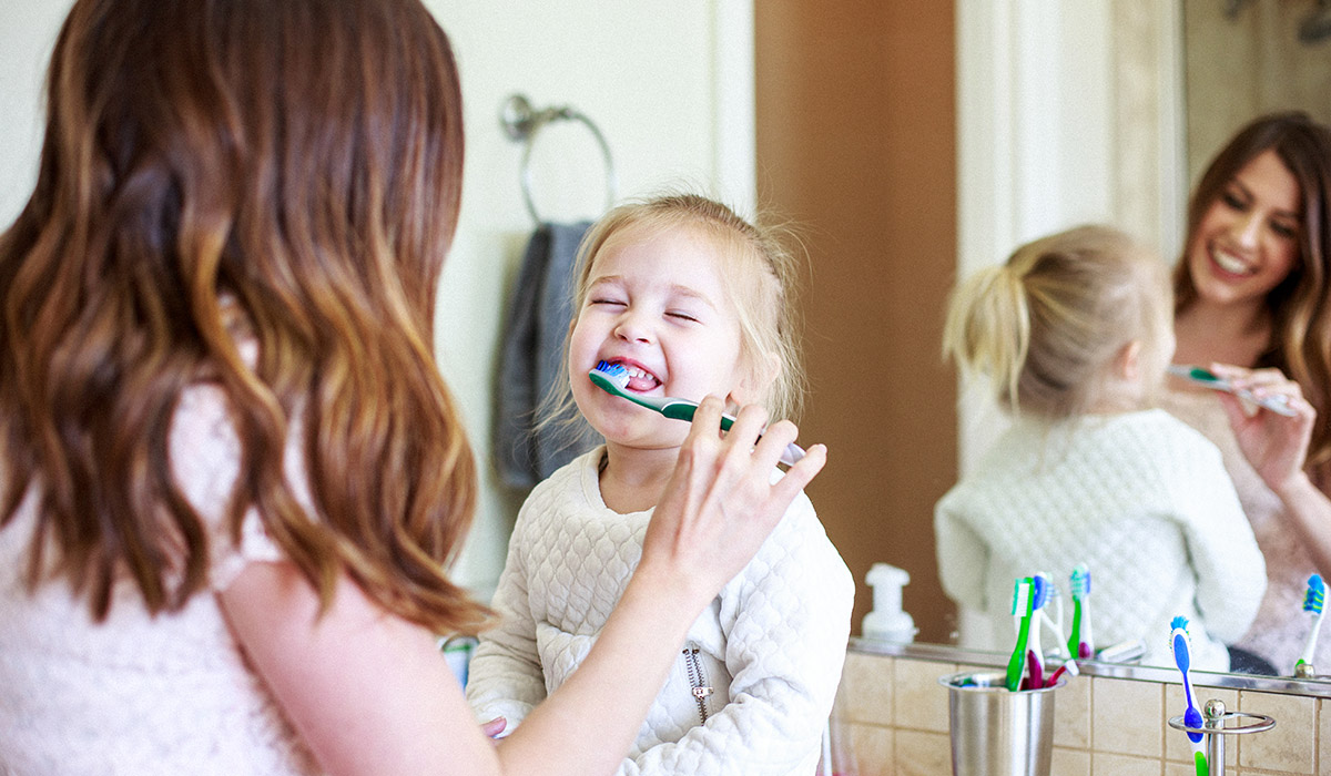 mother helps her toddler daughter brush her teeth