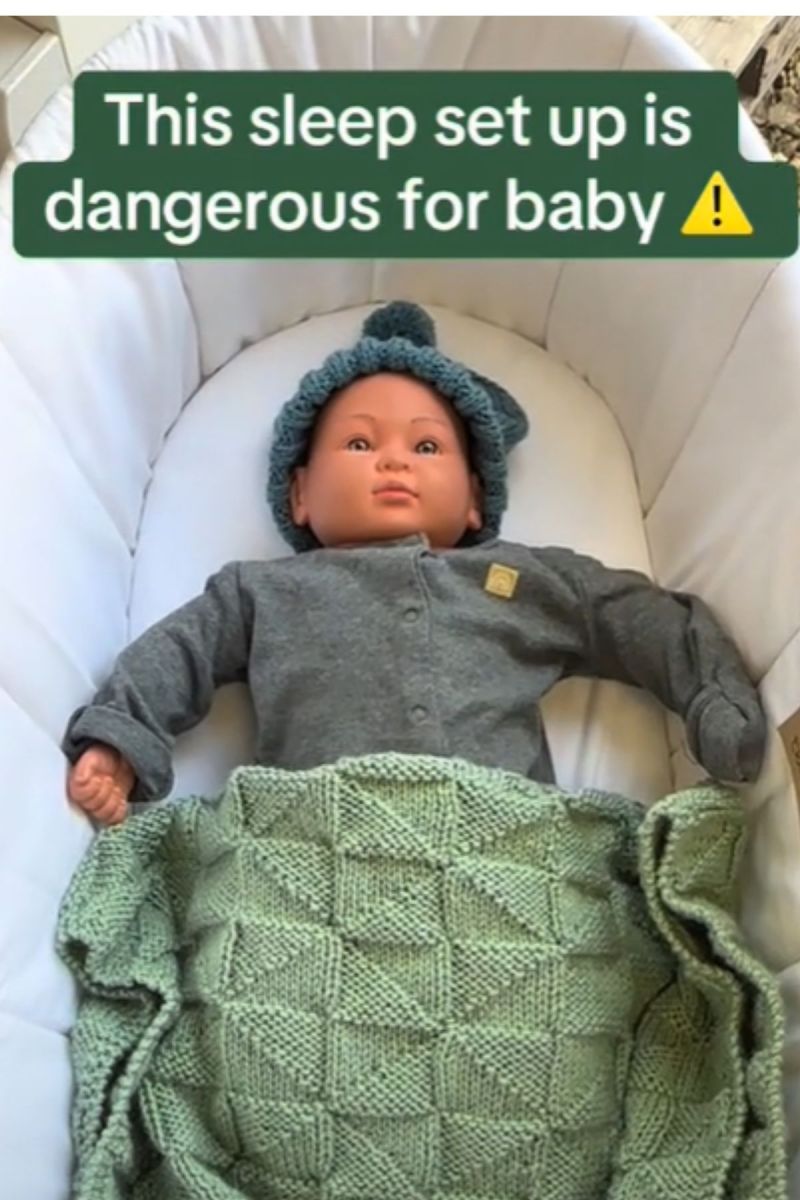 Baby doll asleep in a bassinette with a hat and blanket