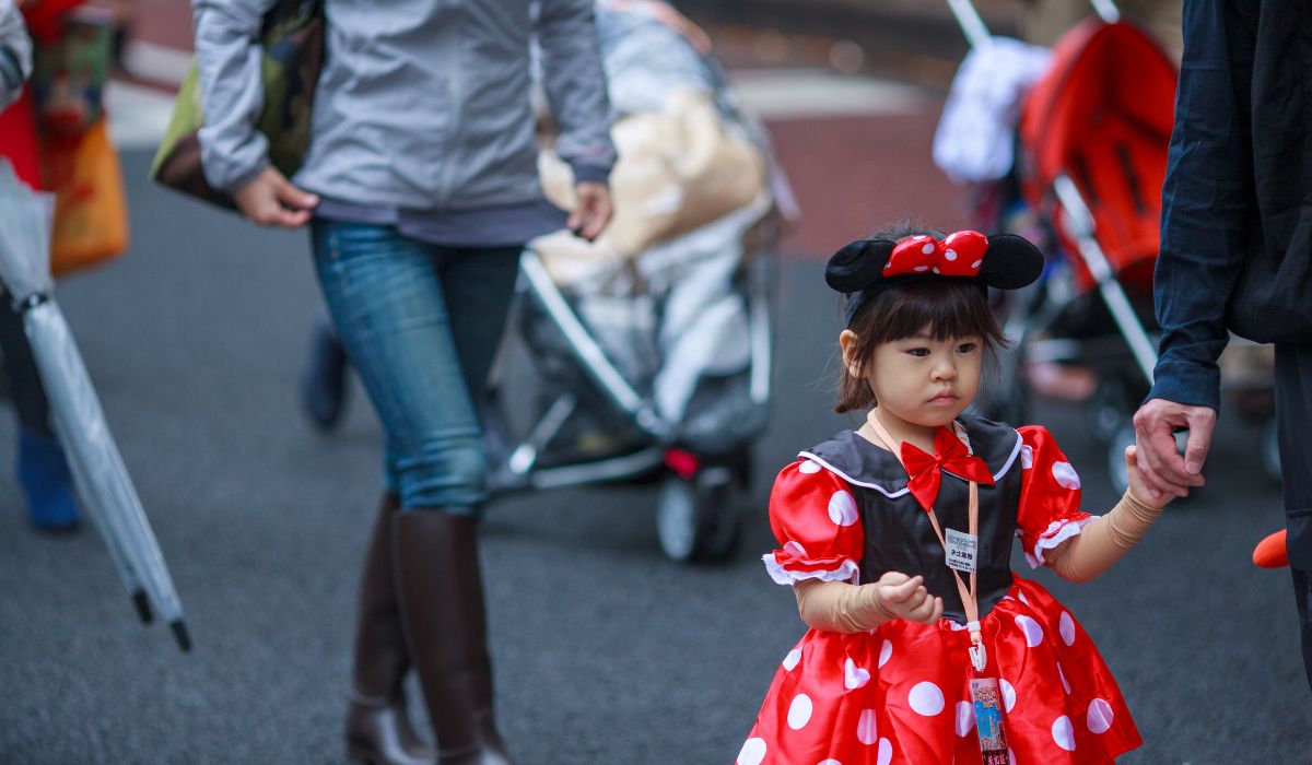 A girl in a costume marching holding hands with her parent.