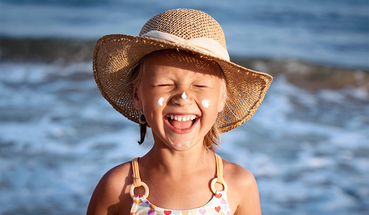 Happy Children Sea Holiday. Smiling Child Girl Sunbathing with Sunscreen on Face in Blue Sea Background. Funny Positive Kid in the Sea