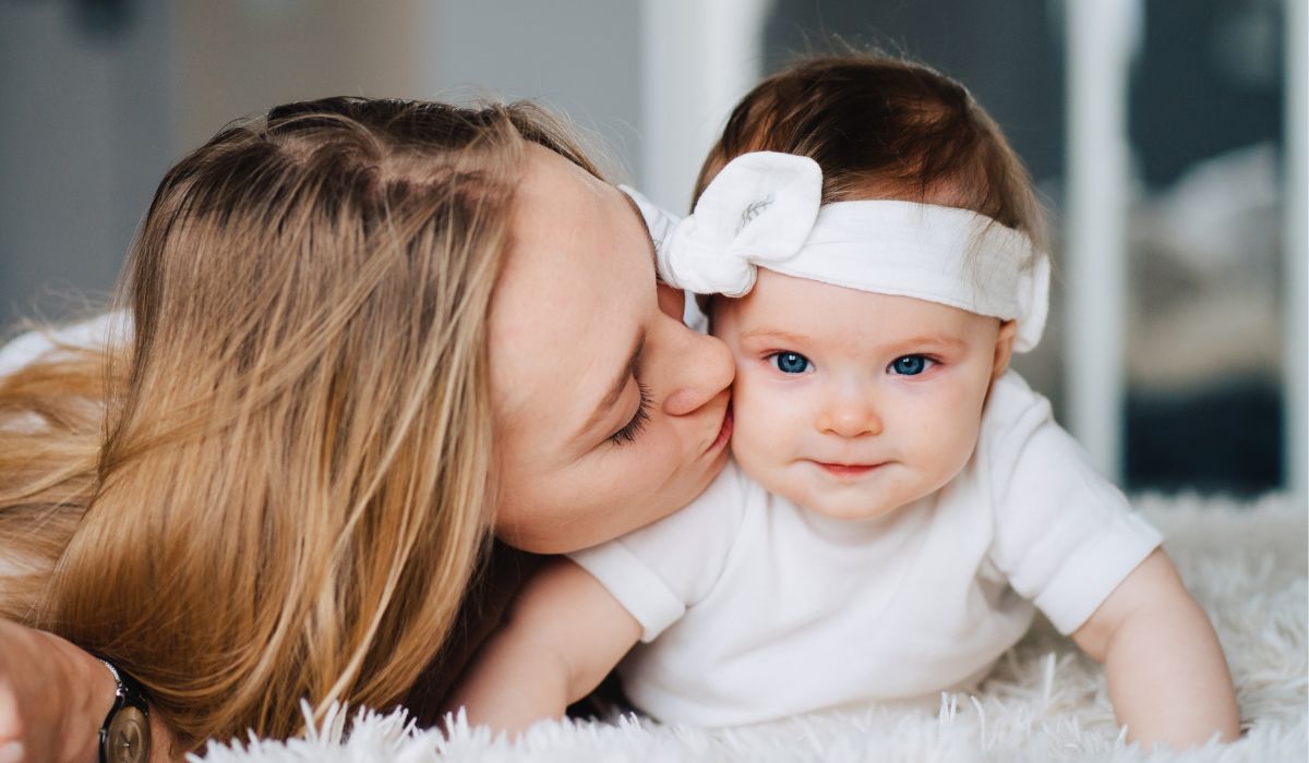 Mum kissing baby on floor wearing a headband