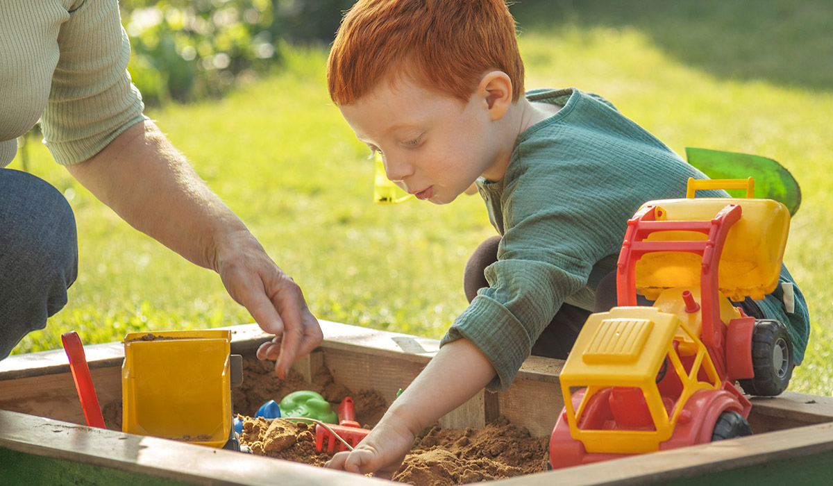 Grandmother playing with grandson in sandbox on sunny day