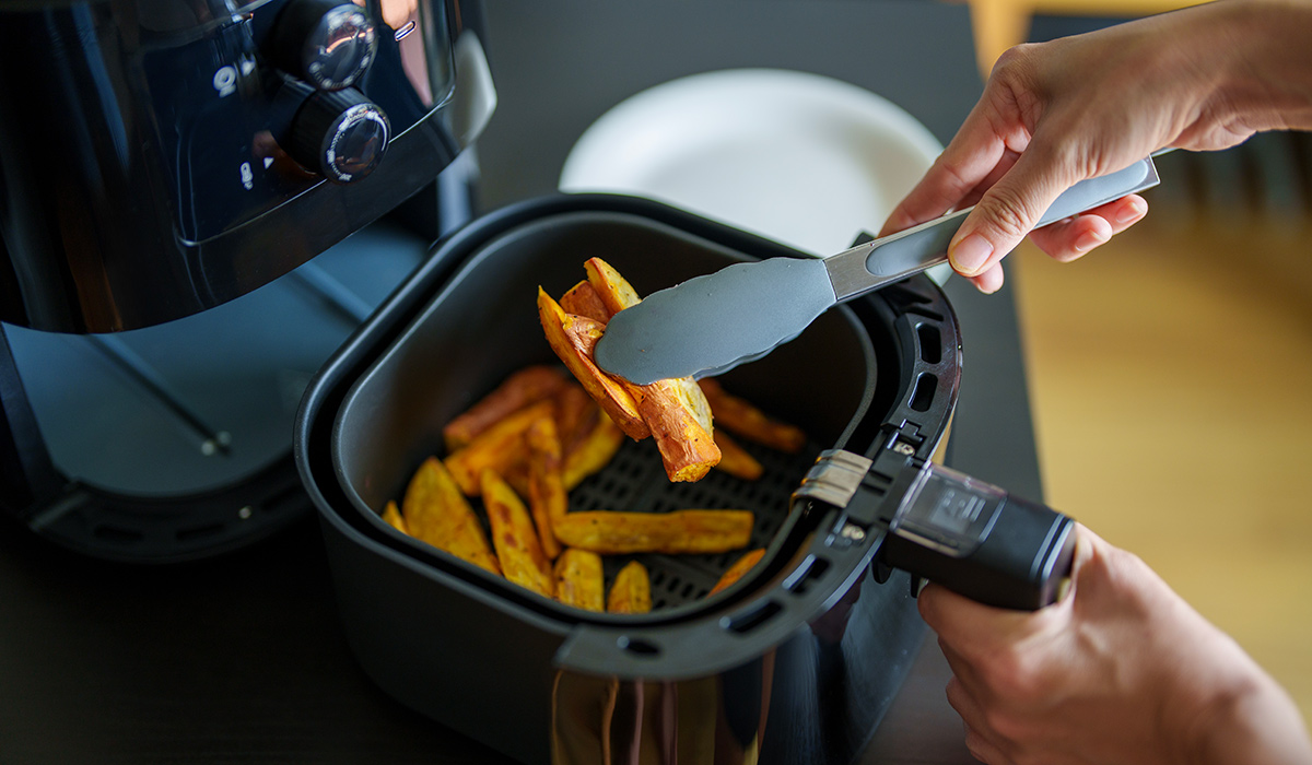 A woman is using an air fryer to prepare food in her kitchen, focusing on a healthier cooking method with minimal oil.