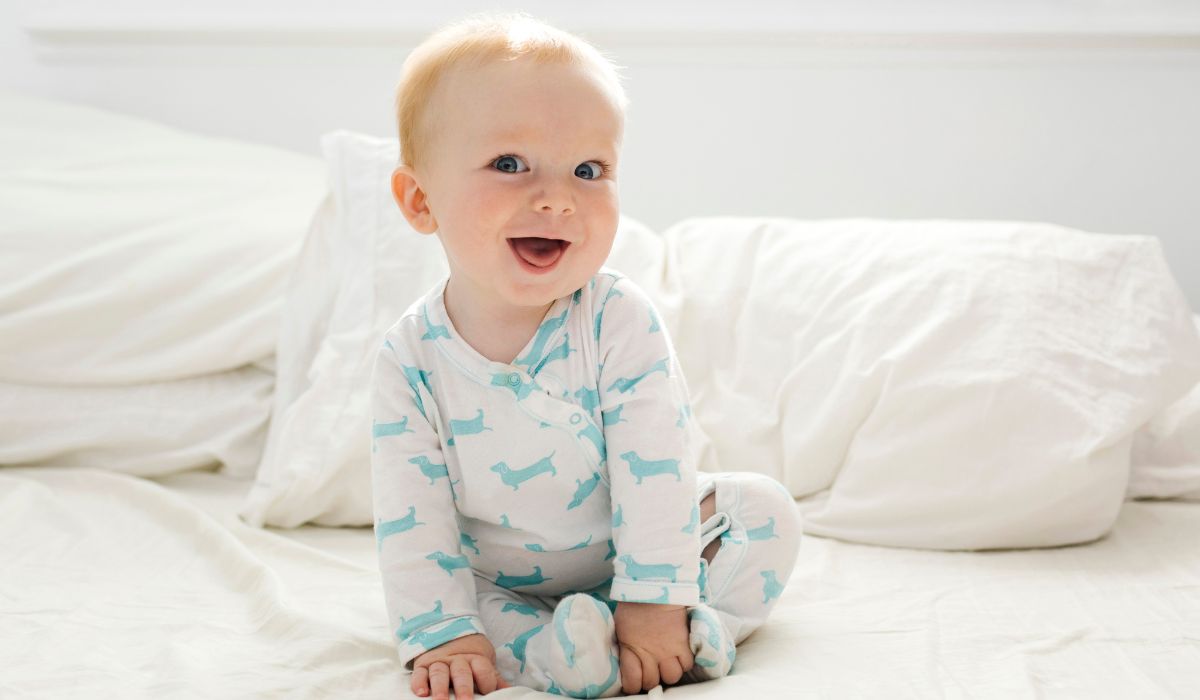 Baby in a babygrow sitting up on a bed