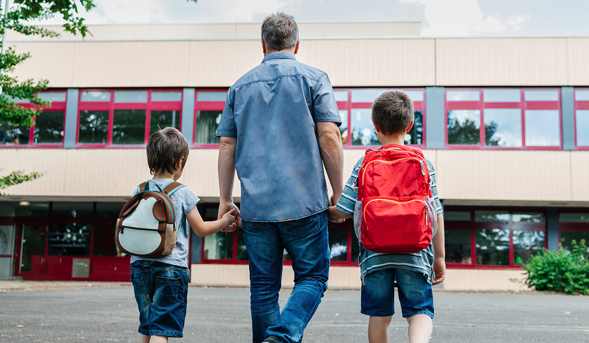 Back to school. View from the back of a happy dad escorts his sons schoolchildren to school. Parental care for children. Pic: Getty Images