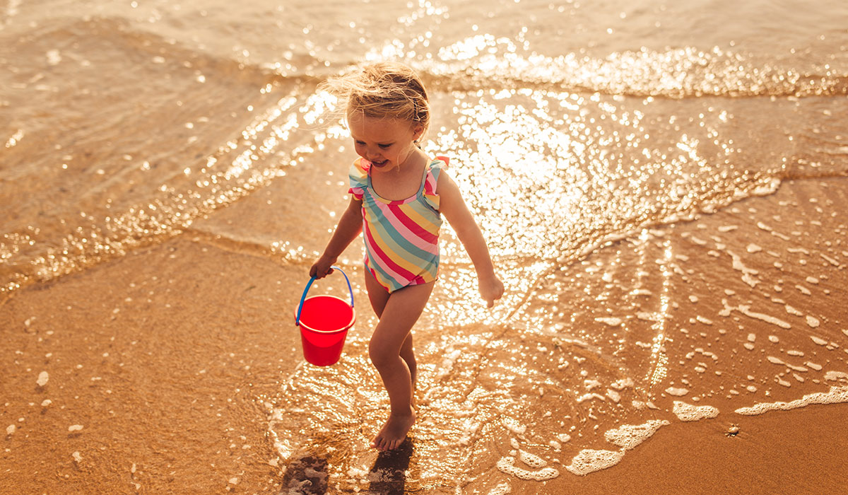 Happy little girl running at shoreline at the beach.