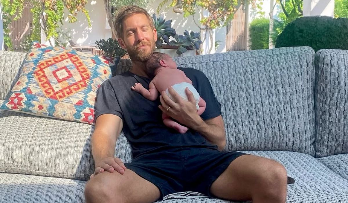 Calvin Harris sitting on a couch holding baby Micah