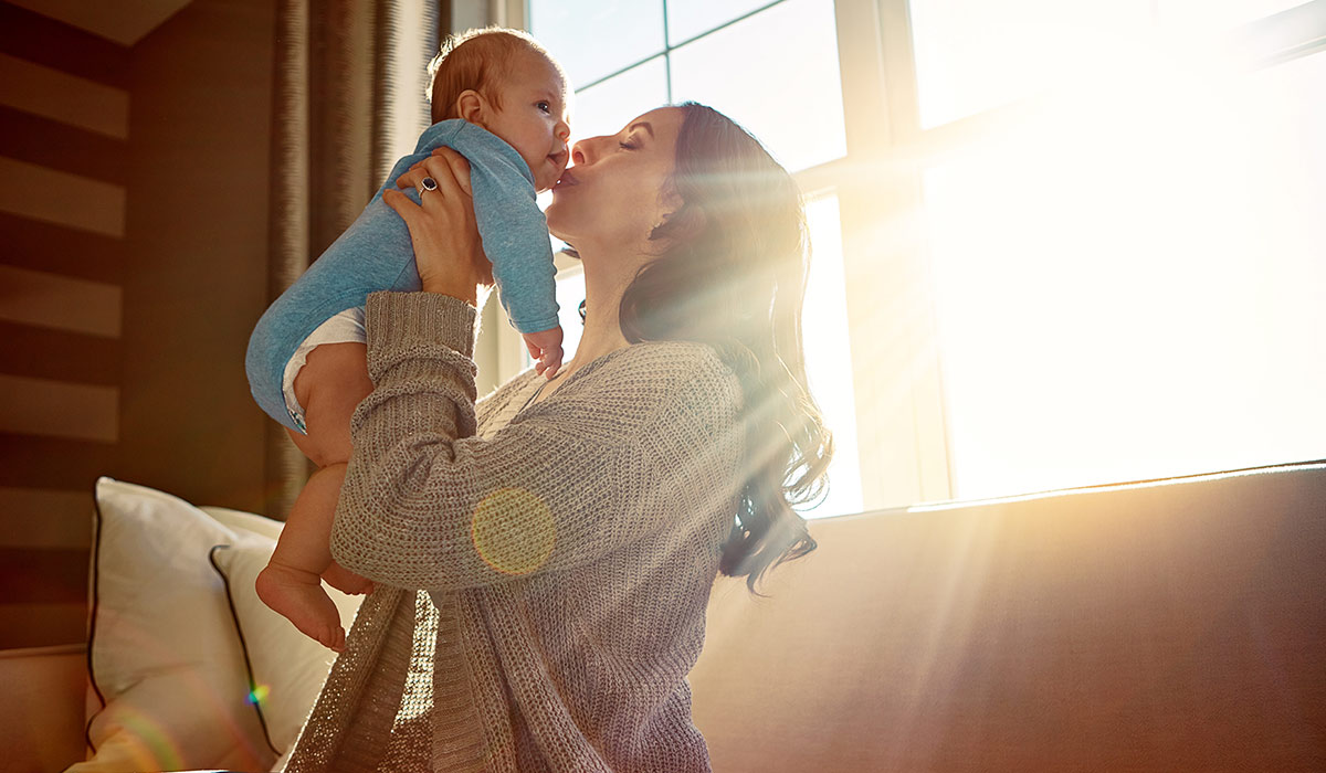 Mother, baby and kiss on cheek in living room on sofa with love for relationship with new born, care. Embrace, light and sunshine for relax on couch with playing, joy and happiness for wellness.; Shutterstock ID 2472681887; purchase_order: -; job: -; client: -; other: -