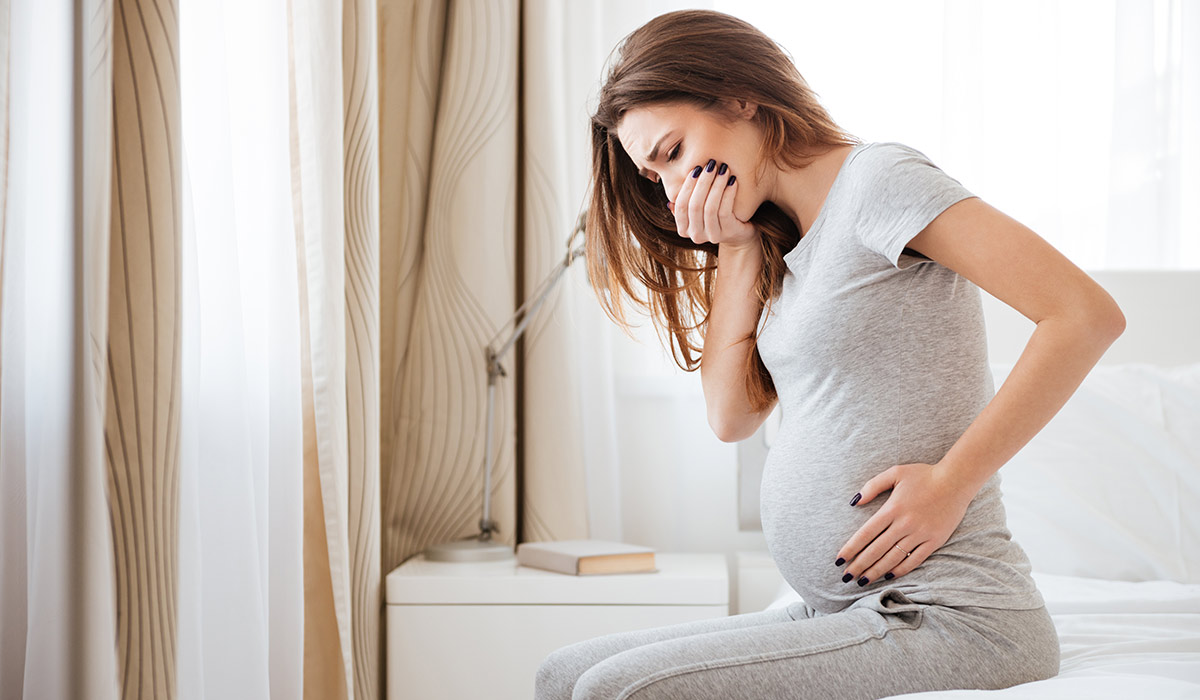 Pregnant young woman sitting on bed and feeling sick at home; Shutterstock ID 613496009; purchase_order: -; job: -; client: -; other: -