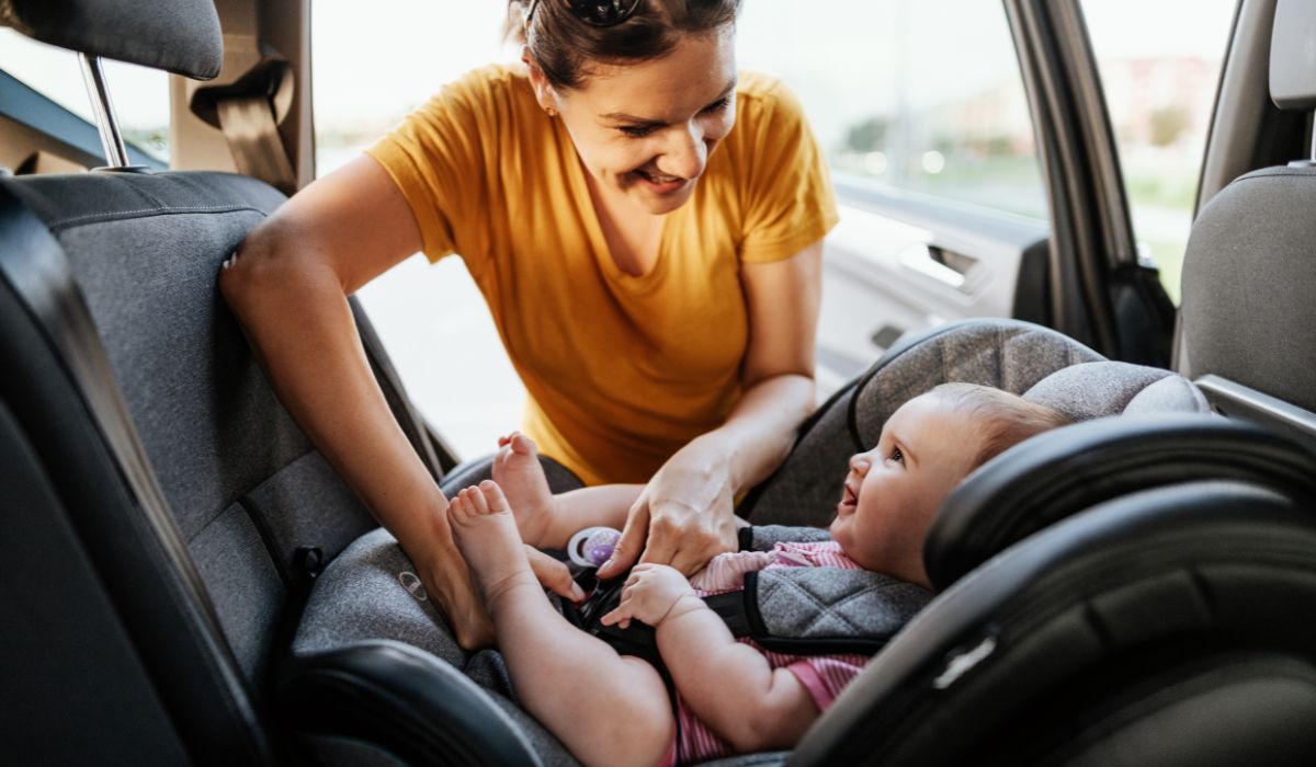 Mother putting her child in their car seat