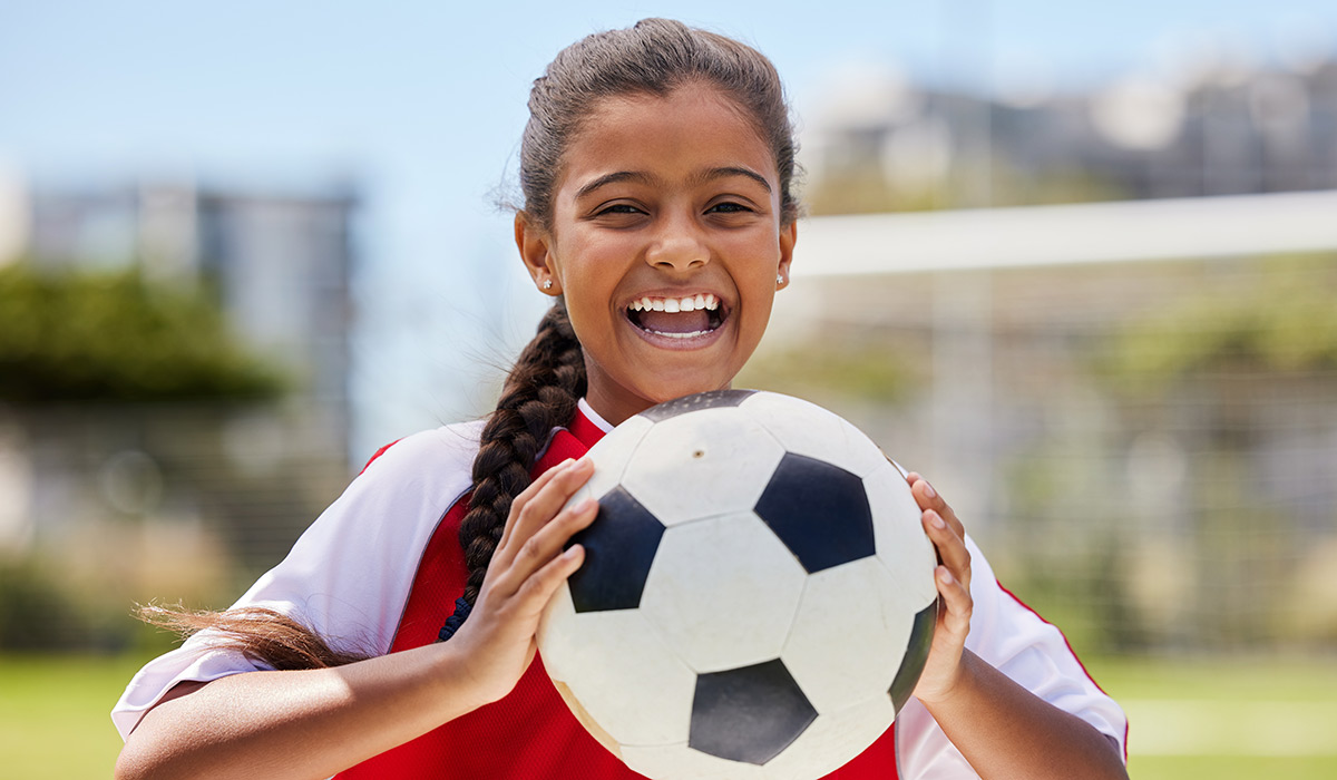 Soccer, sports and happy Indian girl athlete holding a sport ball on a school field. Portrait of fitness, football and exercise of a child smile excited about training, workout and game motivation; Shutterstock ID 2210376937; purchase_order: -; job: -; client: -; other: -