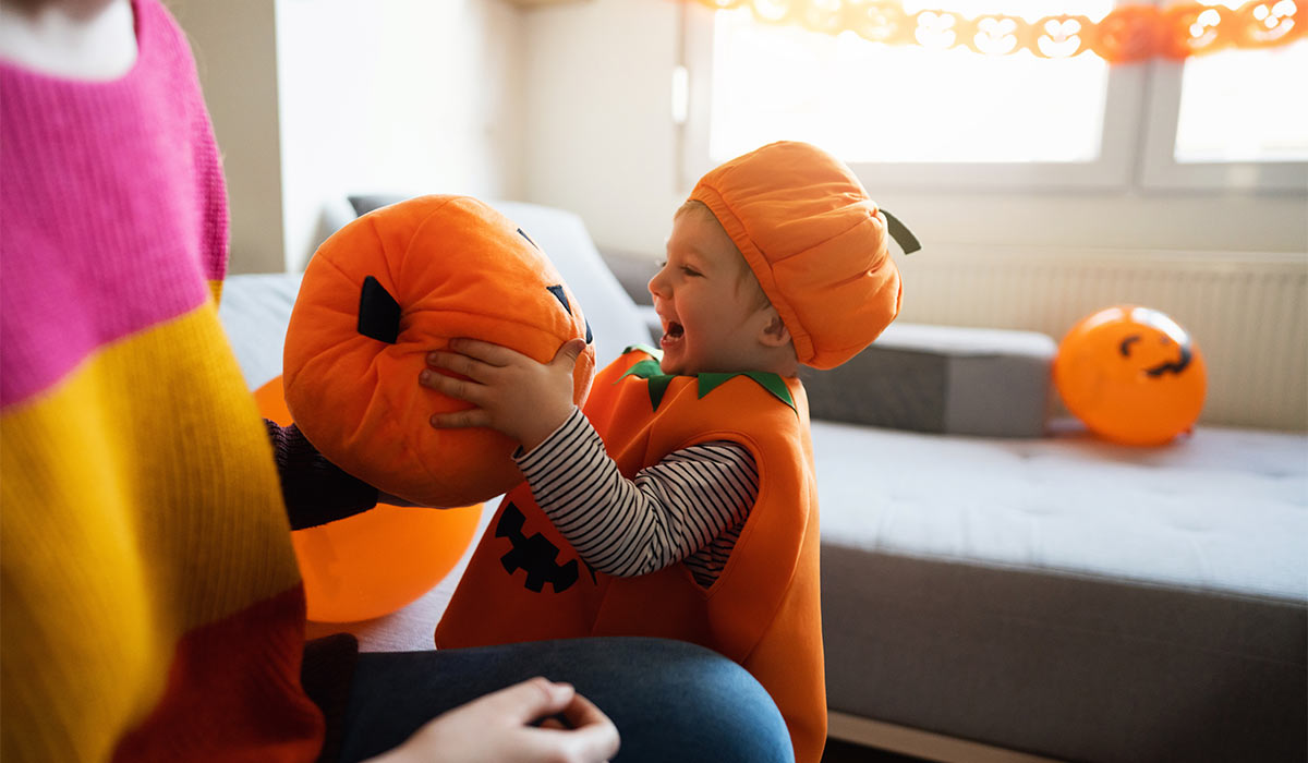 Cute Caucasian toddler boy dressed as a pumpkin, for a Halloween, playing with his mother