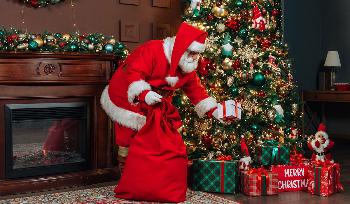santa claus with big bags of gifts puts a gift under the christmas tree. Christmas concept