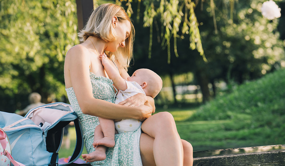 Beautiful mother breastfeeding baby. Young woman breast feeding her newborn baby. Concept of lactation infant, postpartum period, natural motherhood. Mother and baby on nature outdoors.