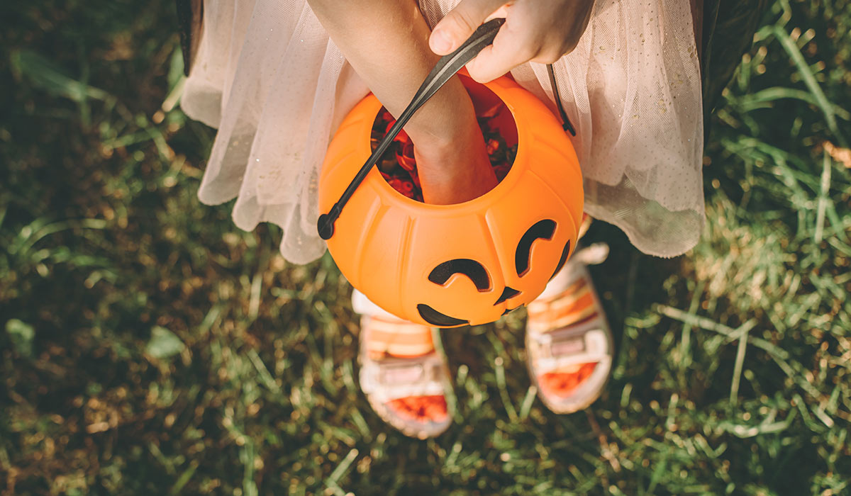 Happy Halloween day. A little cute girl in a witch costume is holding her pumpkin Jack's bucket with candy in her hand. Halloween party, kids trick or treat, close-up.; Shutterstock ID 2519243899; purchase_order: -; job: -; client: -; other: