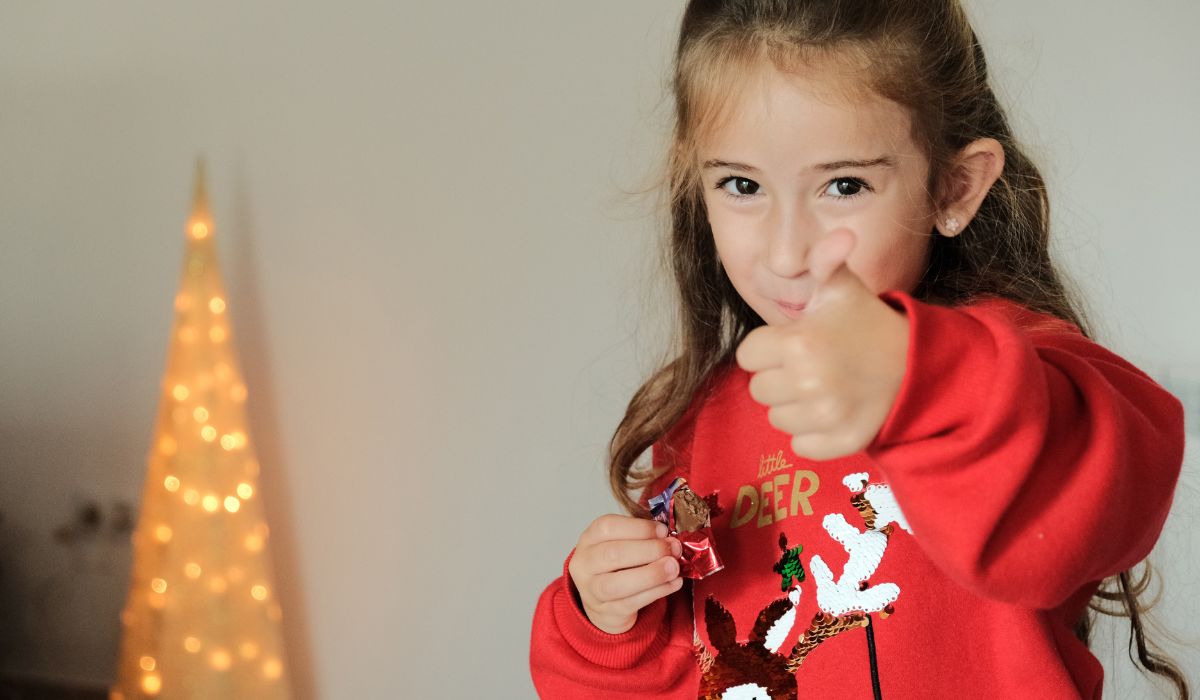 Little girl eating chocolate and wearing Christmas jumper