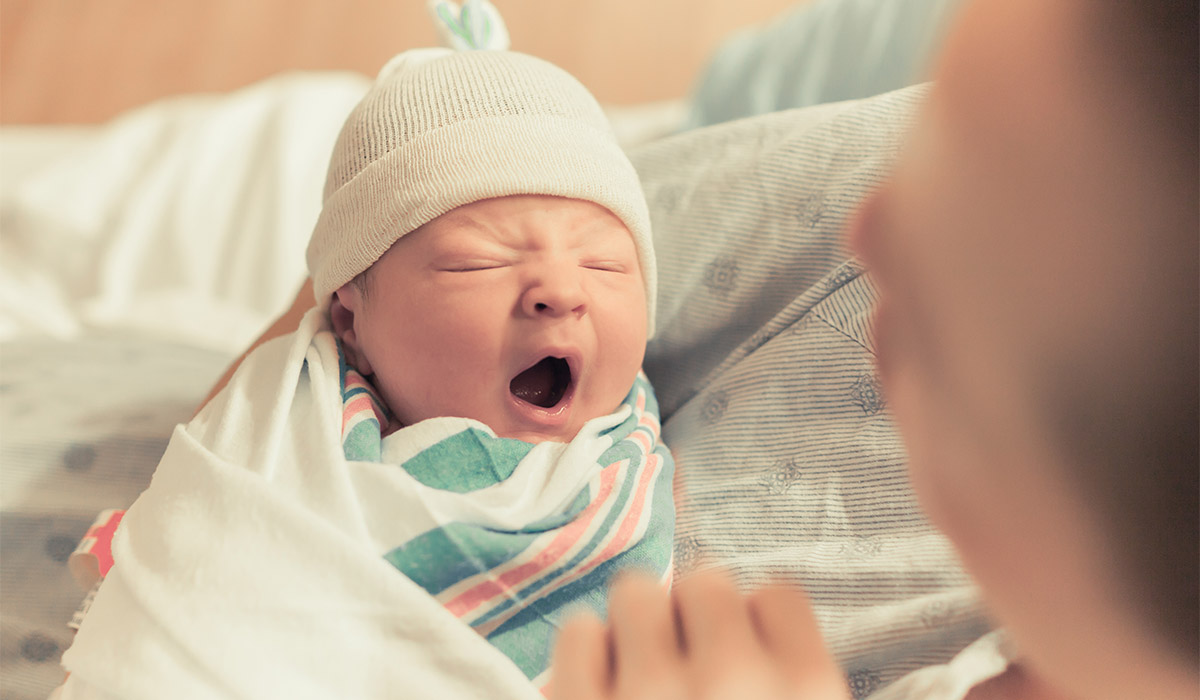 Mother holding cute newborn baby boy in her arms. Sleepy baby yawning