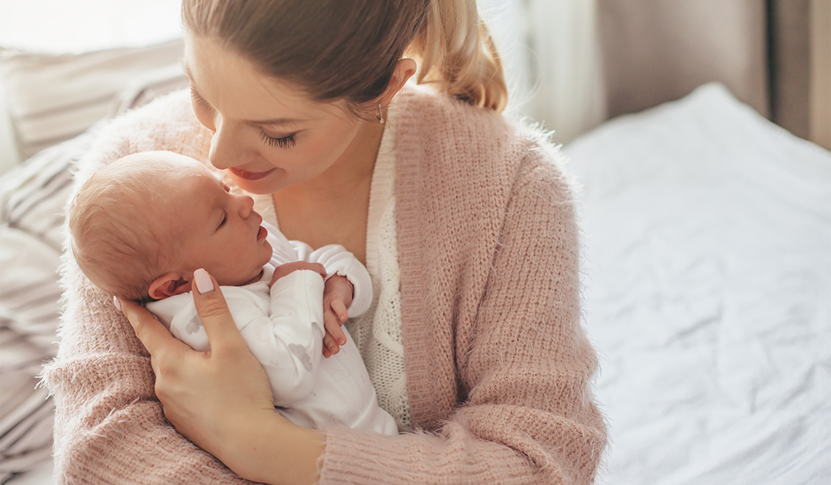 Home portrait of a newborn baby with mother on the bed. Mom holding and kissing her child.; Shutterstock ID 1050001412; purchase_order: -; job: -; client: -; other: