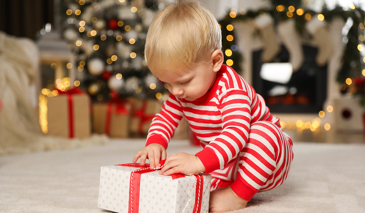 Cute baby in Christmas pajamas unpacking gift box at home; Shutterstock ID 2696082045; purchase_order: -; job: -; client: -; other: