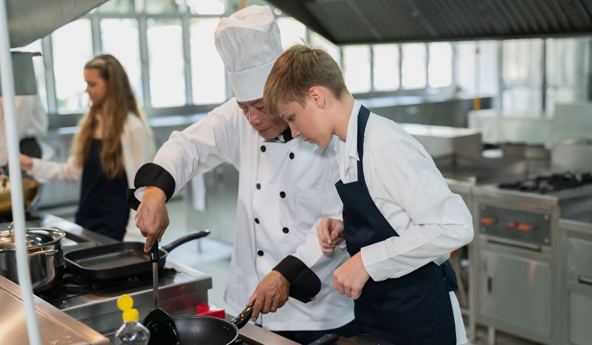 Teen boy working with chef in kitchen